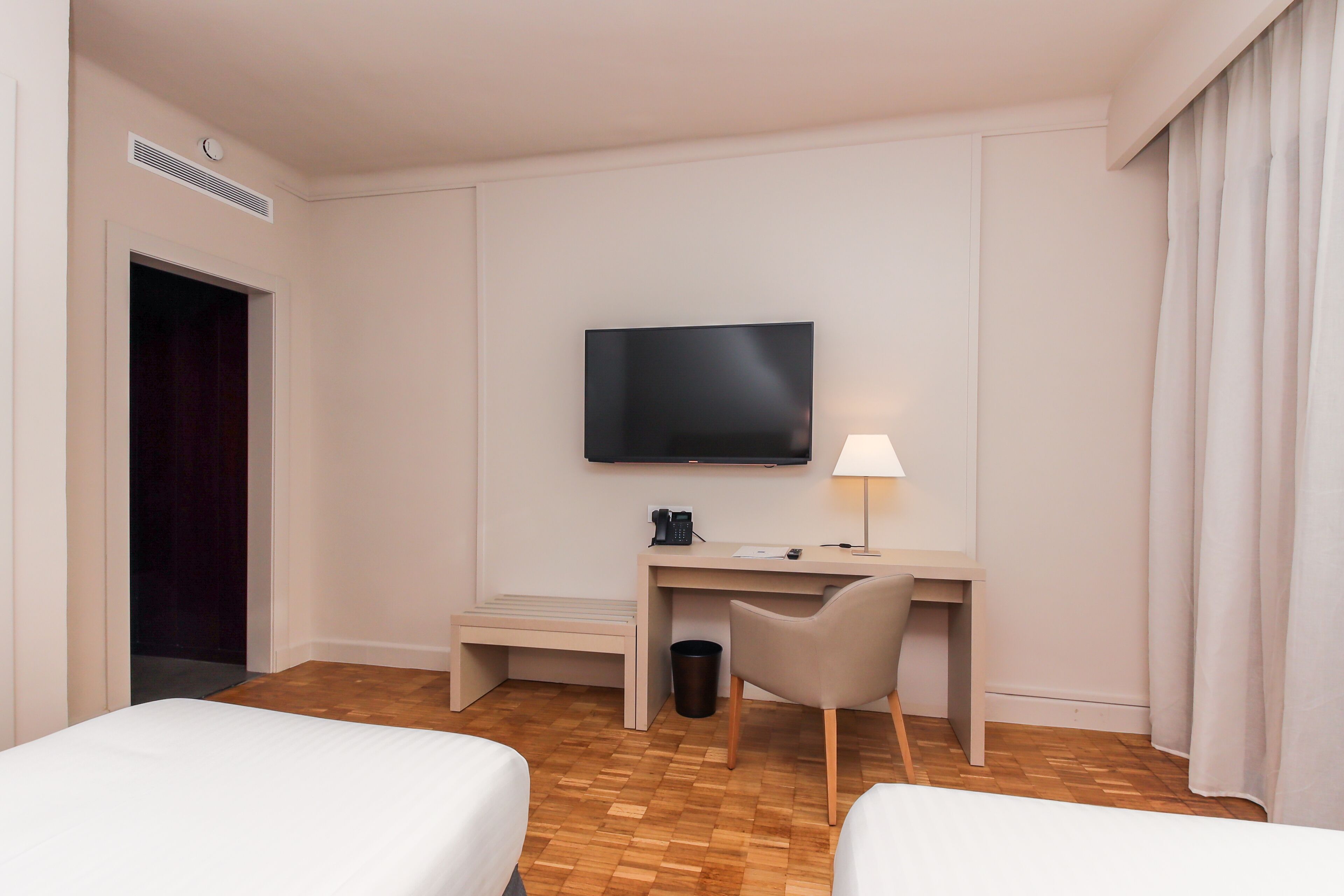 A hotel room with a bed, a desk with a chair, a television, and a waste bin.