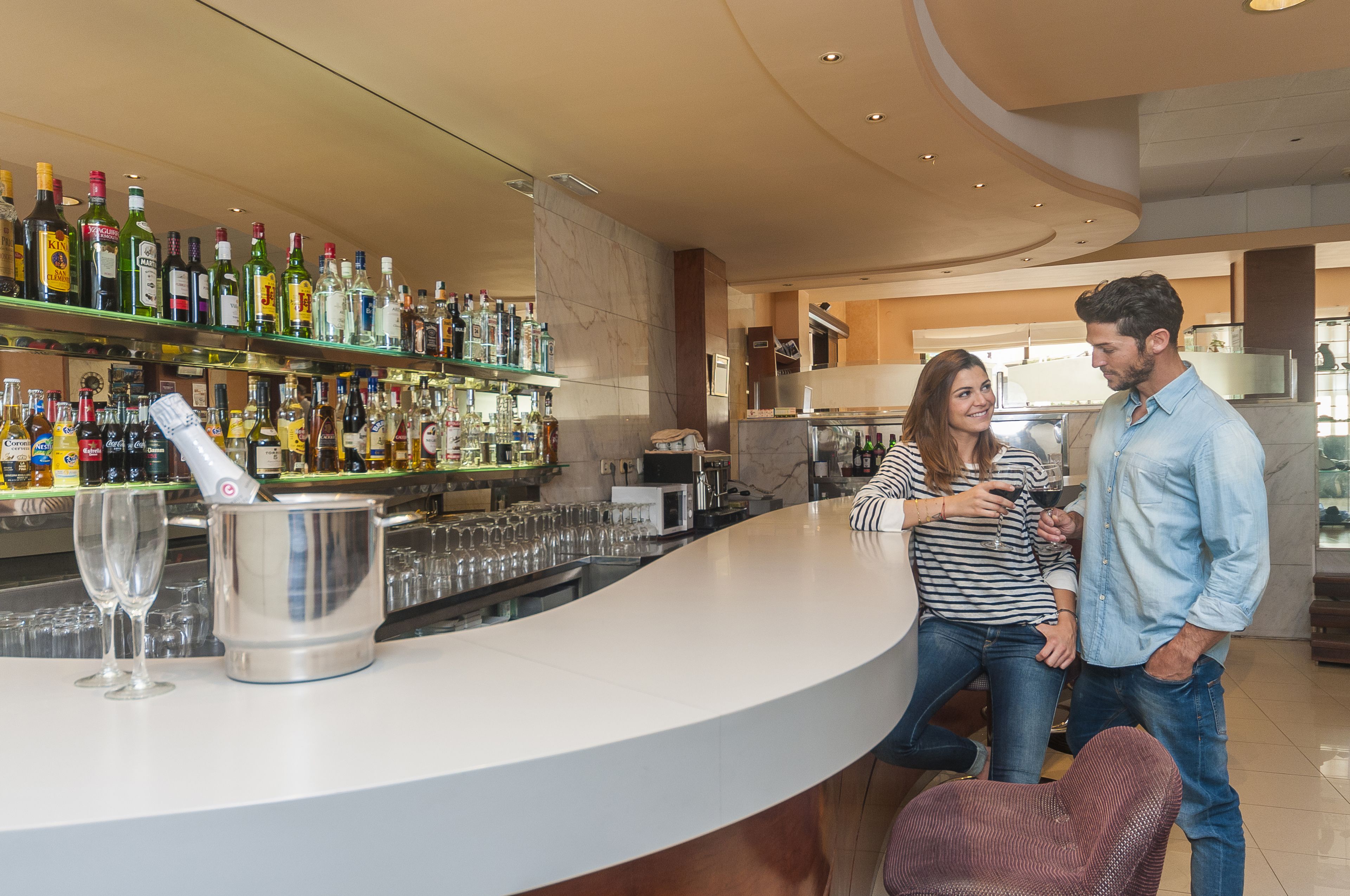 A bar area with a curved counter, a variety of liquor bottles, and a large metal container.