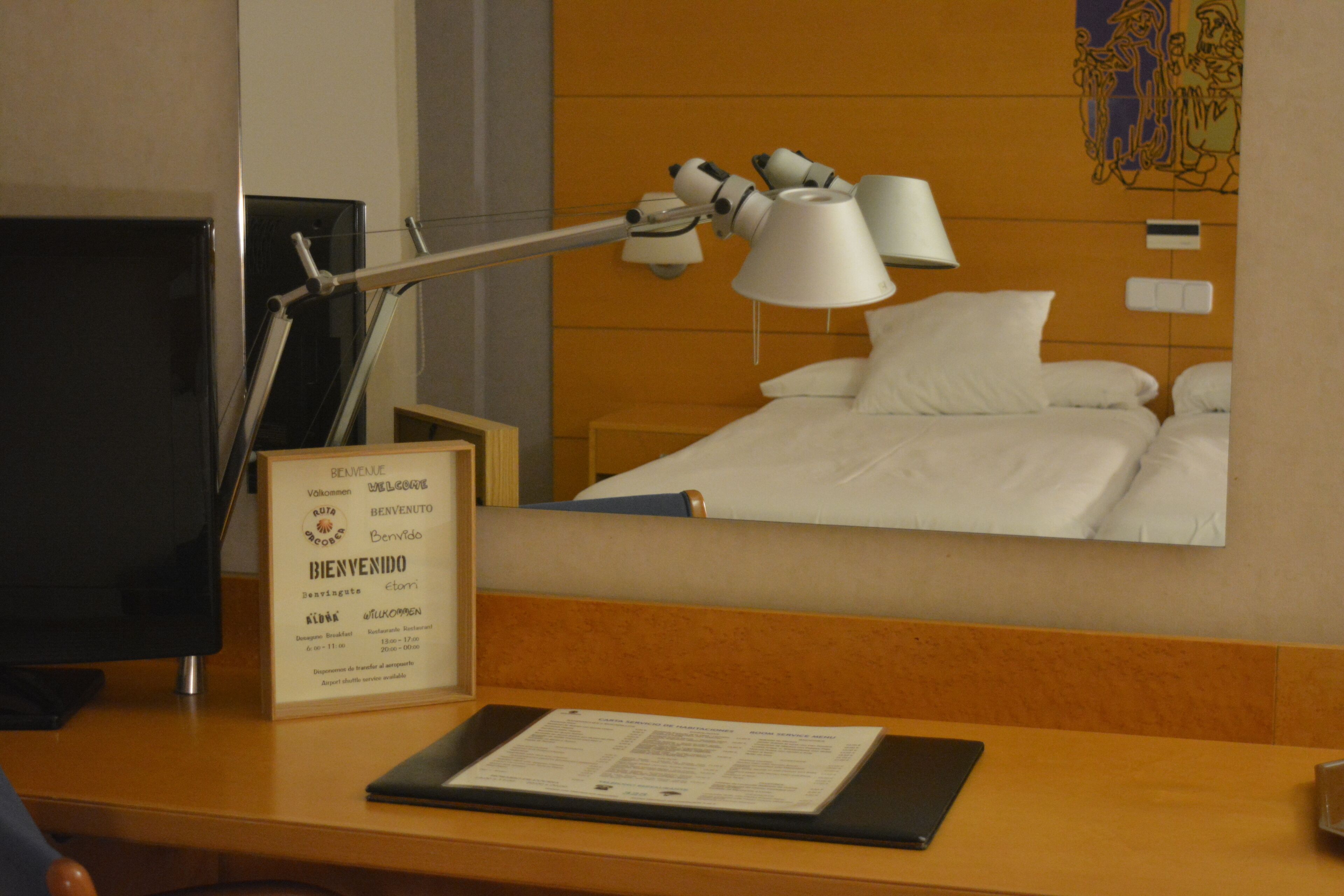 A hotel room with a bed, a desk with a computer and a lamp, and a welcome sign.