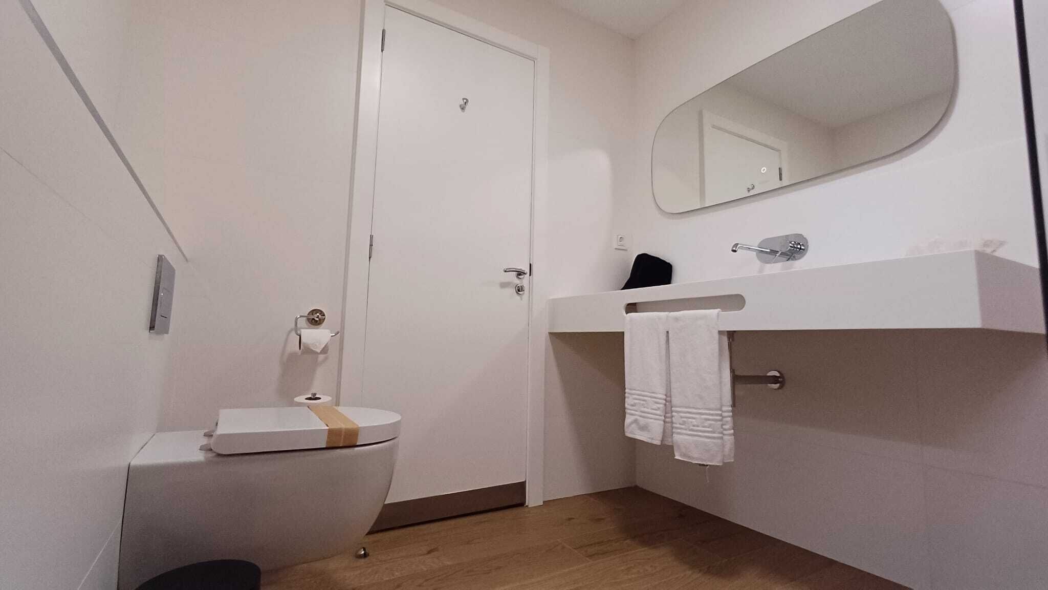 Un baño pequeño y limpio con inodoro, lavamanos, espejo y toallero.