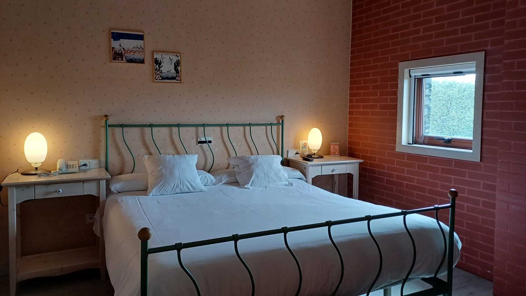 Une chambre à coucher comprenant un lit, deux tables de chevet, une commode, une fenêtre et deux lampes fixées au mur.