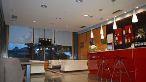 A modern bar area with red bar stools, a counter with various bottles, and a large window offering a view of the outside. - Ruta Jacobea (Santiago de Compostela)
