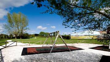 Un parc avec une balançoire, un terrain herbeux et un bâtiment orné d’une banderole.