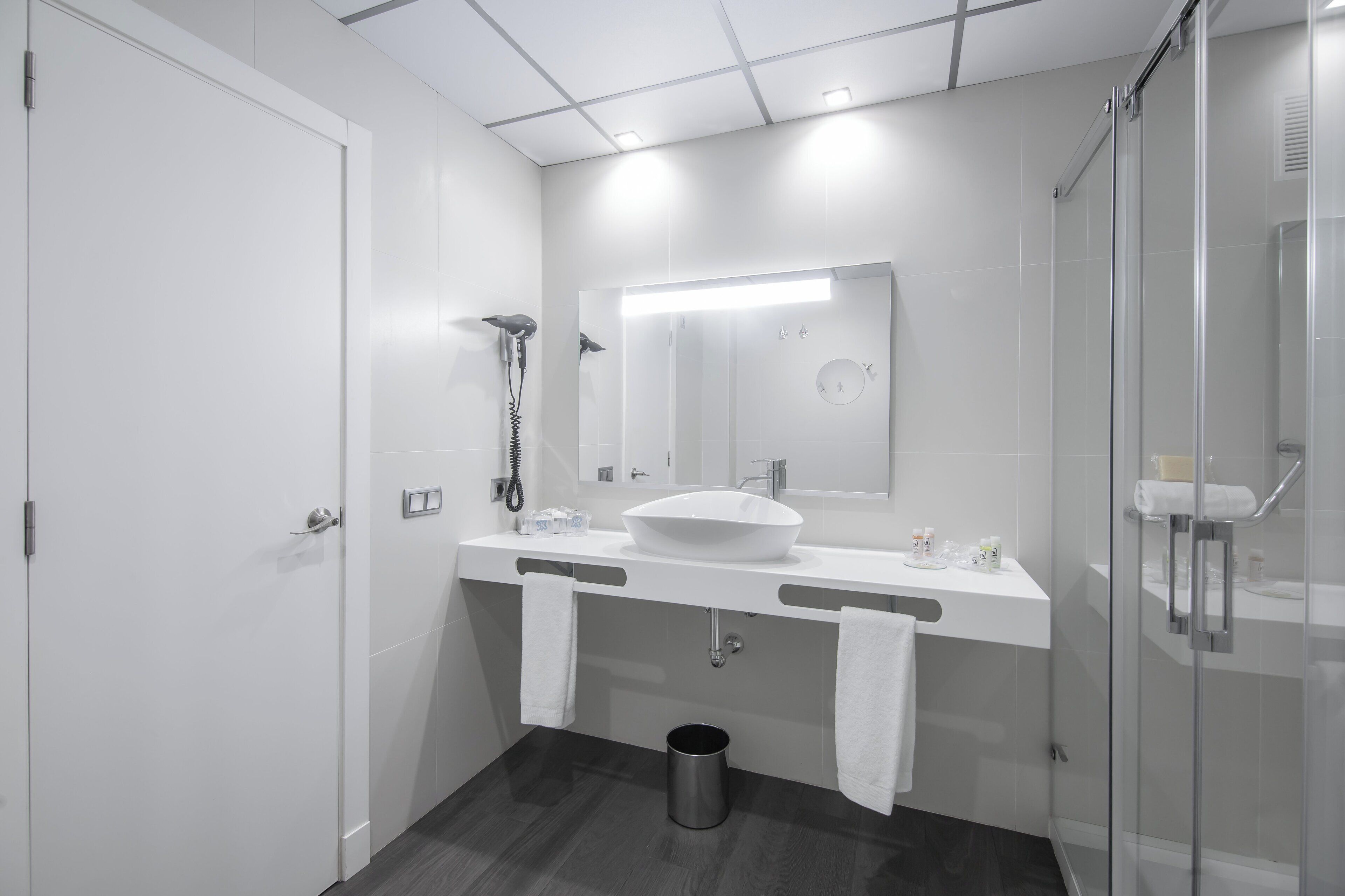 Un baño moderno con un lavamanos blanco, un espejo grande y una cabina de ducha de vidrio.