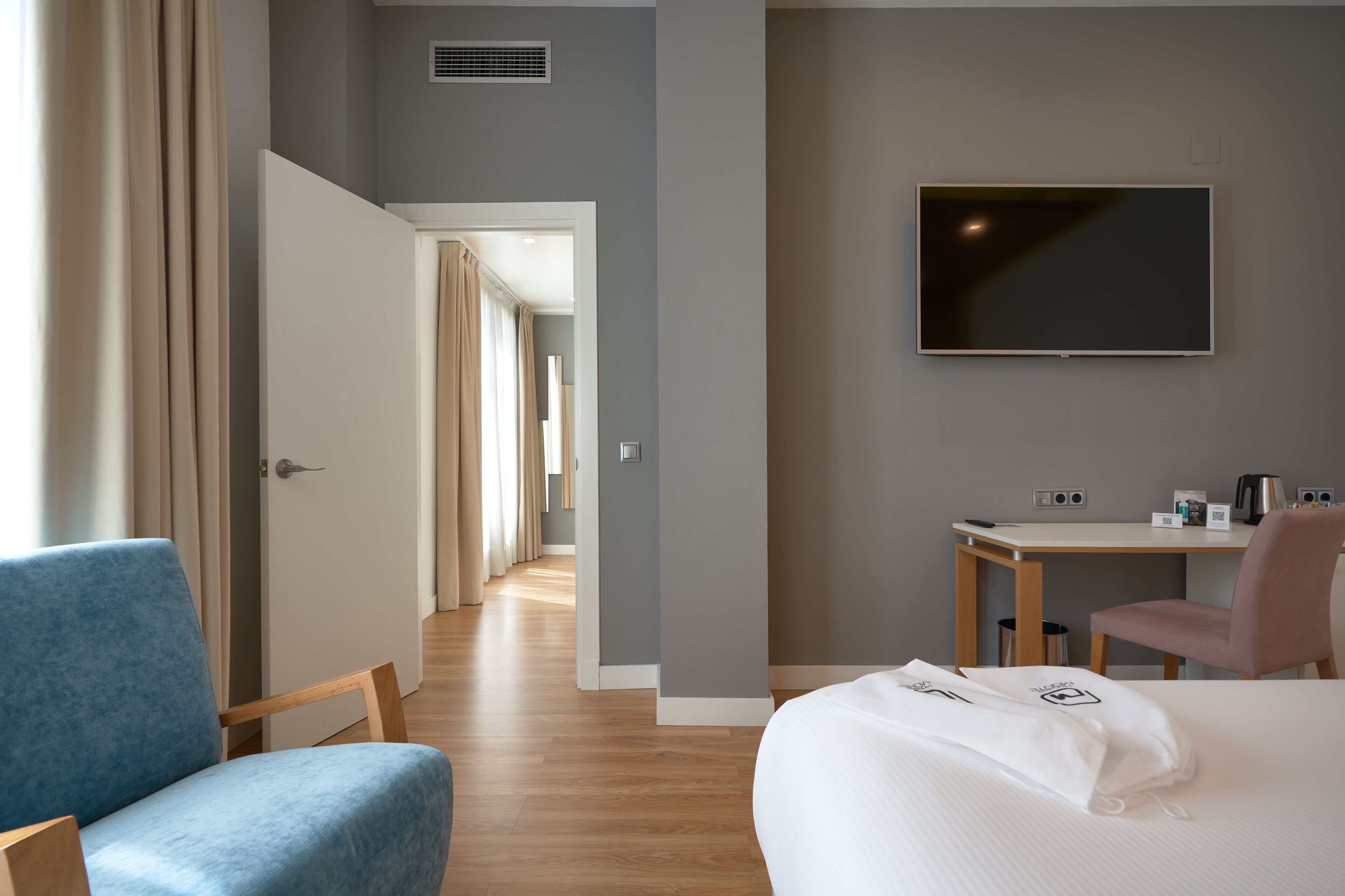 Une chambre d’hôtel avec un lit, un bureau, une chaise et un téléviseur fixé au mur.