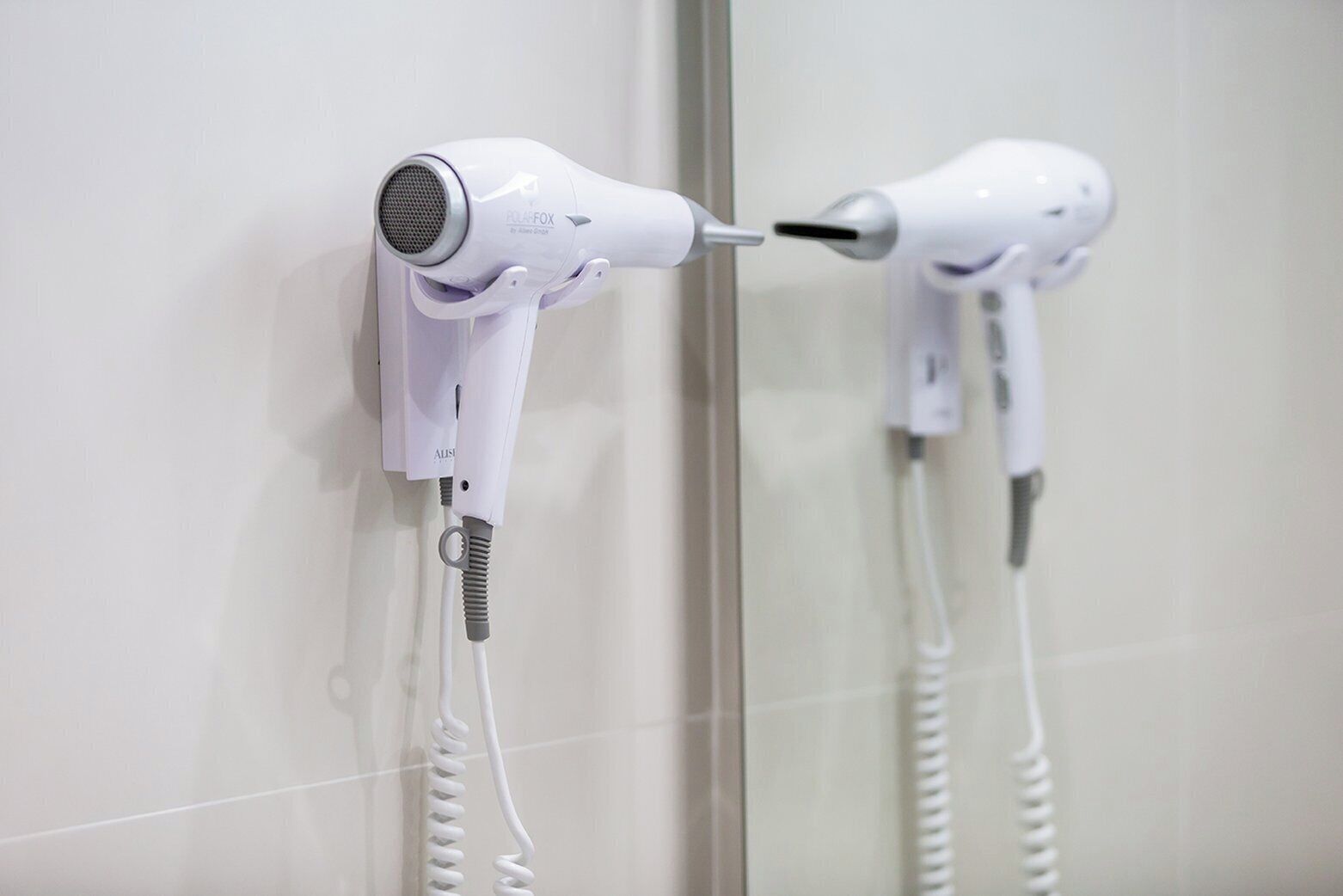 Un sèche-cheveux fixé au mur avec un cordon.