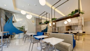 Un restaurante moderno con mesas y sillas blancas, detalles azules y plantas colgantes.