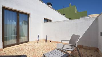 Una terraza en la azotea con un muro blanco, una puerta corredera de vidrio y un ventanal pequeño. Se observan dos sillas blancas y una mesa.