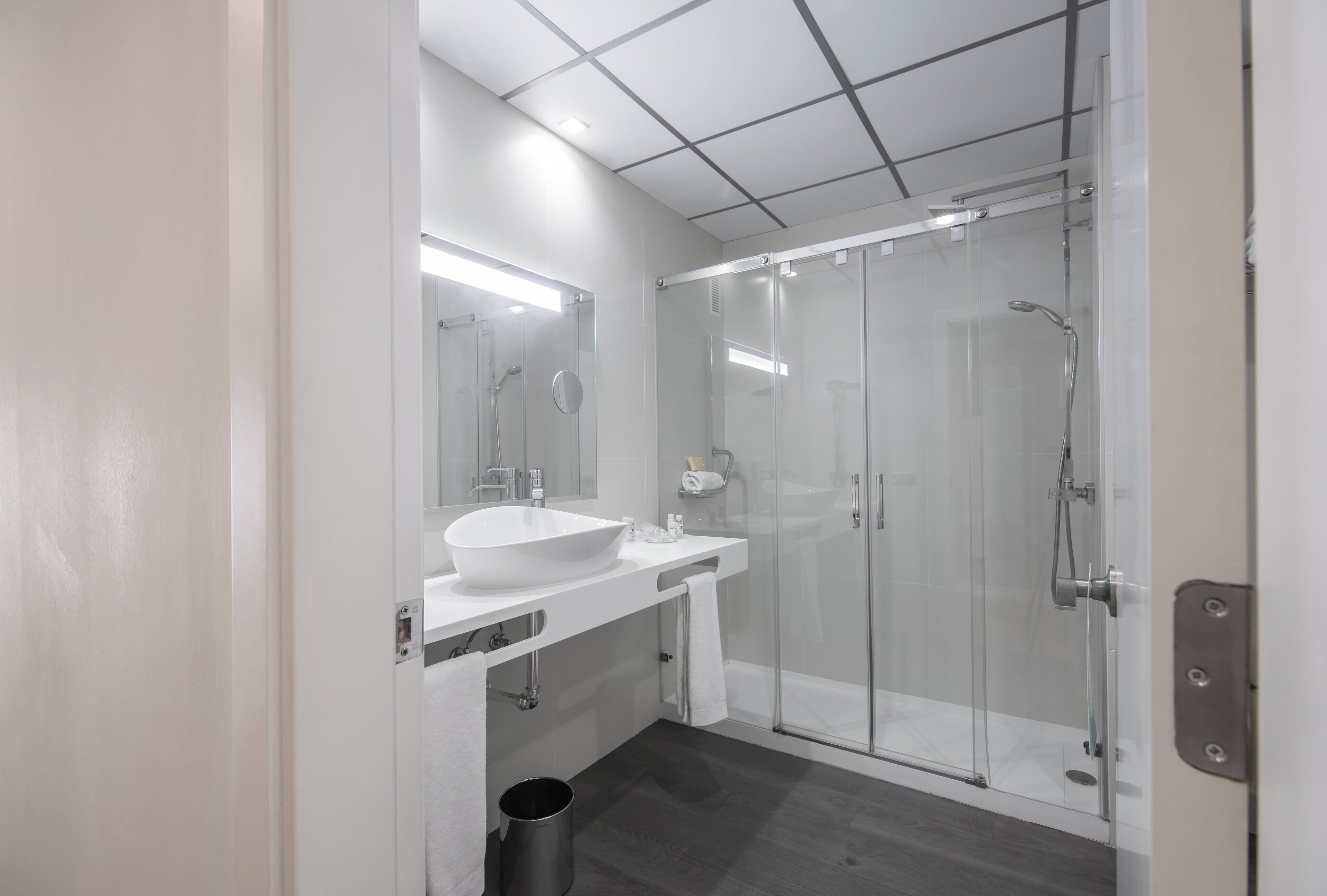 A modern bathroom with a white sink, mirror, and glass shower enclosure.
