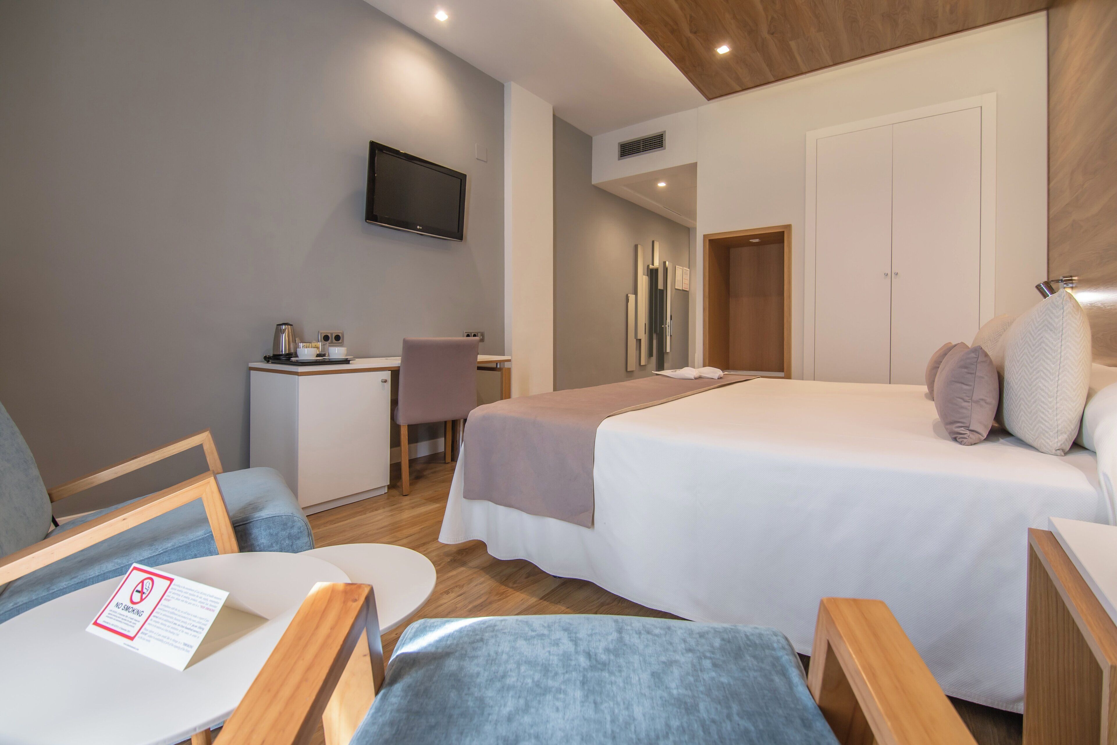 A hotel room with a bed, a desk, a chair, a TV mounted on the wall, and a door.