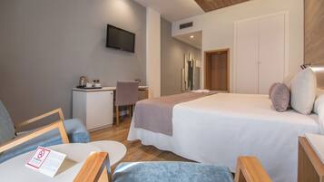 A hotel room with a bed, a desk, a chair, a TV mounted on the wall, and a door.