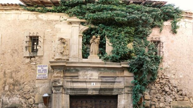A historic building with a stone facade, a wooden door, and a statue above the entrance. - Posada de San José (Cuenca)