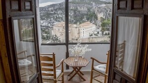 A balcony with a table and two chairs, overlooking a mountainous landscape with buildings. - Posada de San José (Cuenca)