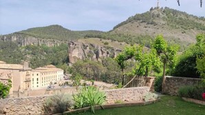 A grassy courtyard with a stone wall, a building with multiple windows, and a mountainous backdrop. - Posada de San José (Cuenca)