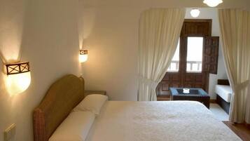 Habitación de hotel con una cama grande, una mesita pequeña y vistas al exterior a través de cortinas.