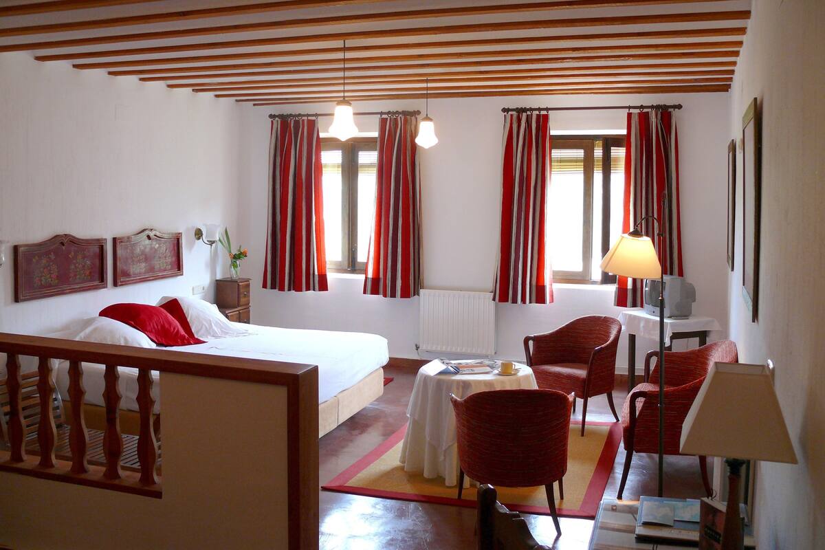 A hotel room with a bed, a desk with a chair, a table, and a window with curtains.
