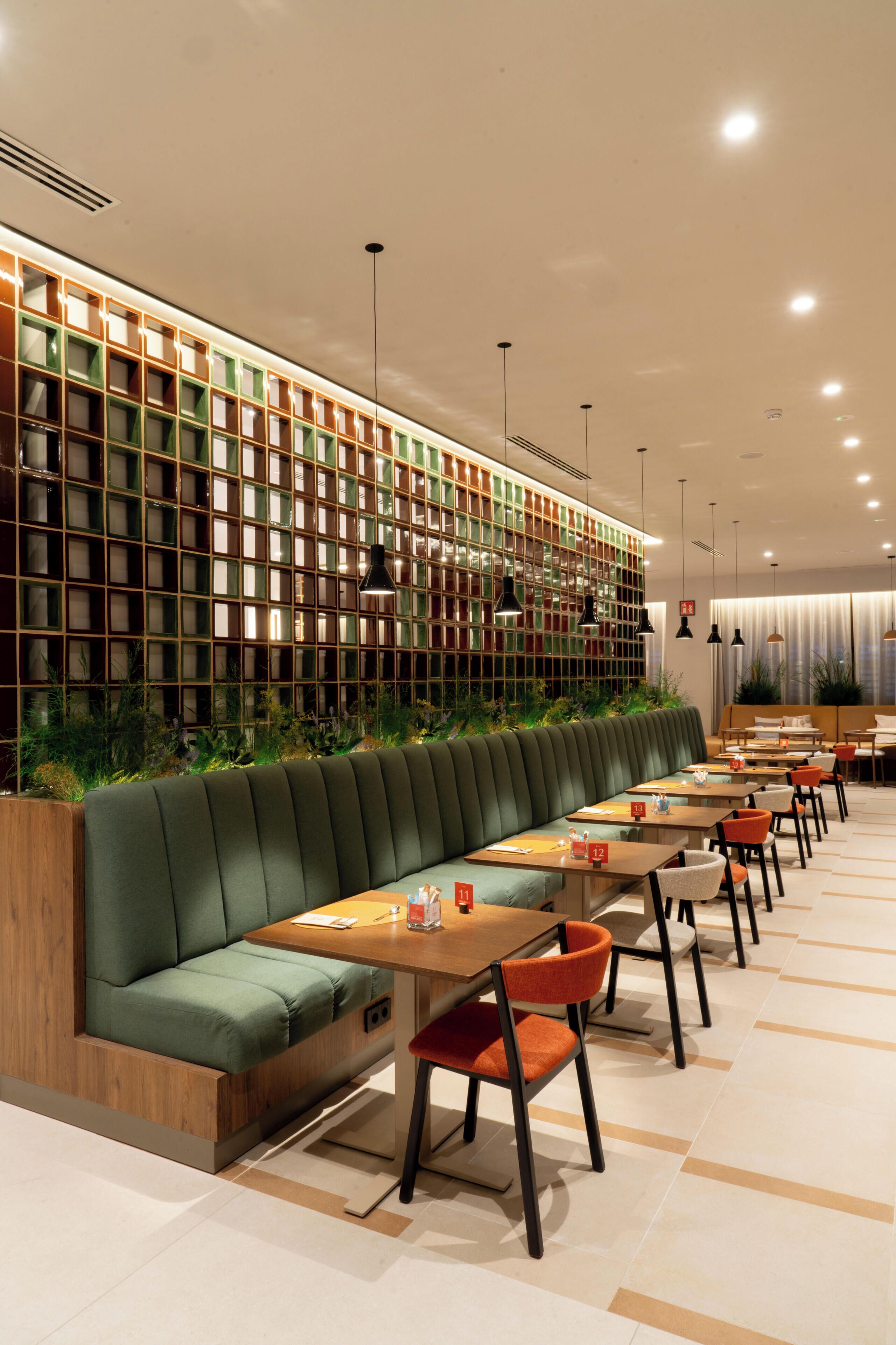 Un restaurante moderno con una amplia zona de asientos tipo banco, mesas e iluminación colgante.