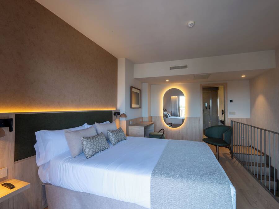 A modern hotel room with a large bed, a desk, and a chair.