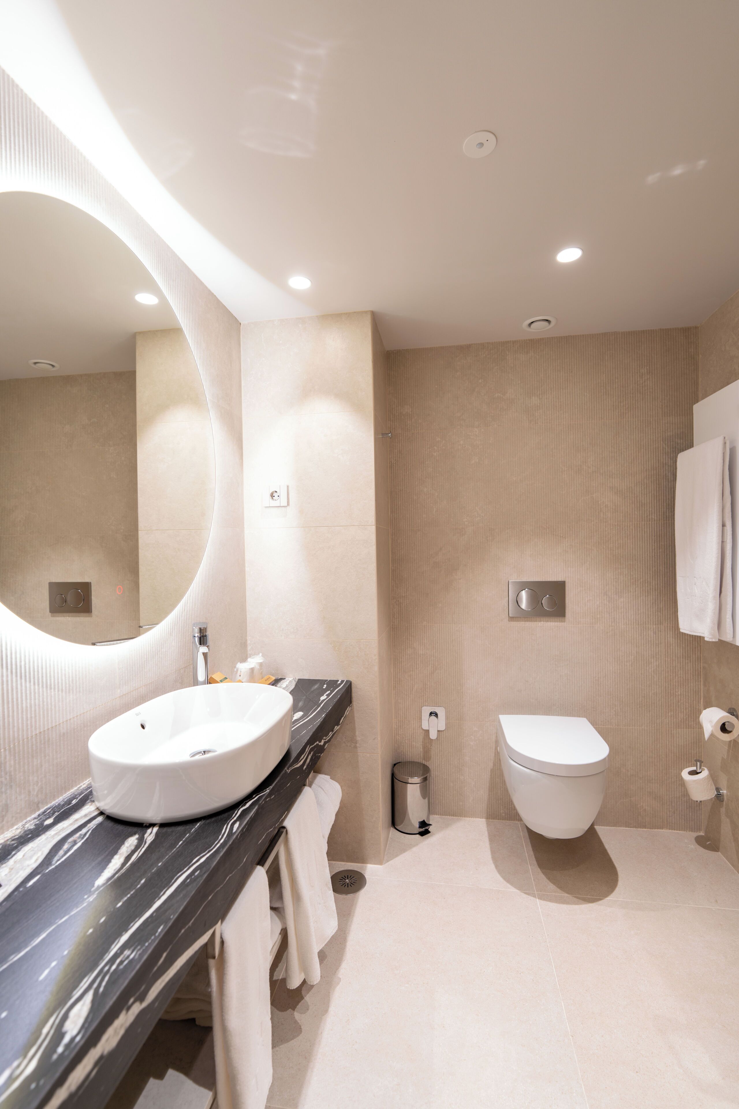 A modern bathroom with a large mirror, a white sink, a toilet, and a towel rack.