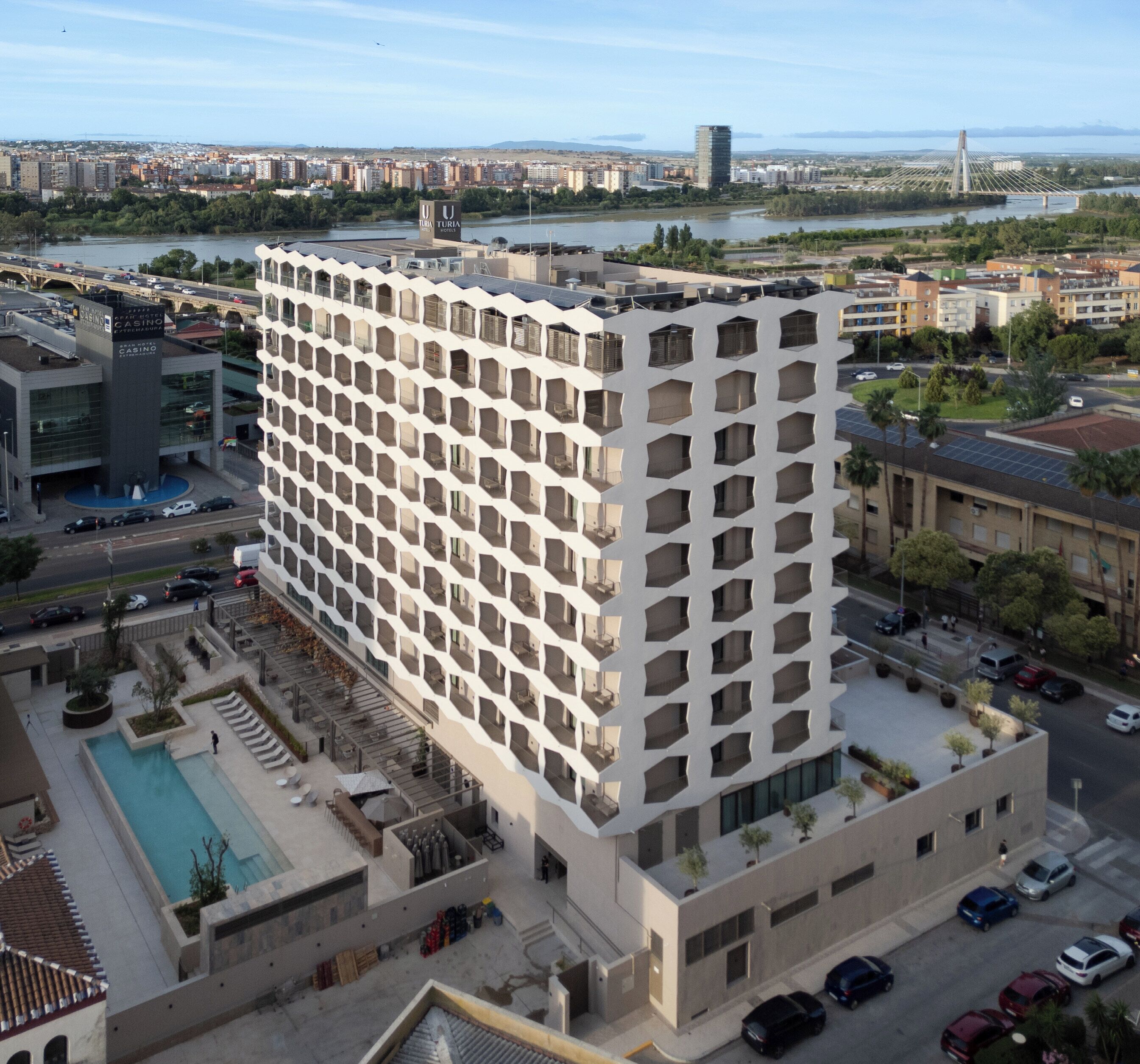 Un hotel de varios pisos con una fachada geométrica llamativa, una piscina y vistas a la ciudad.