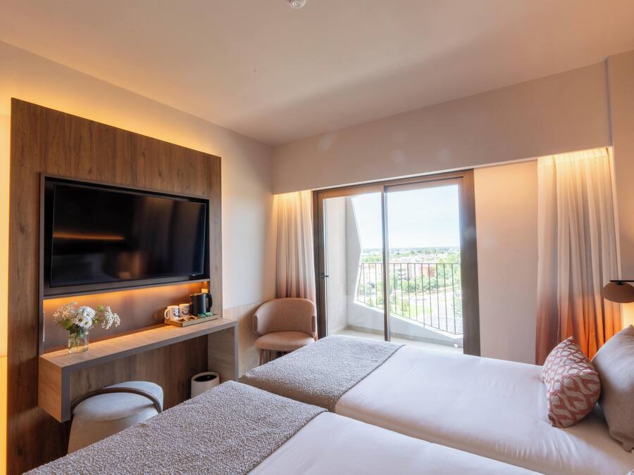 Une chambre d’hôtel équipée d’une télévision, de deux lits, d’un bureau, d’une chaise et d’un balcon avec vue.