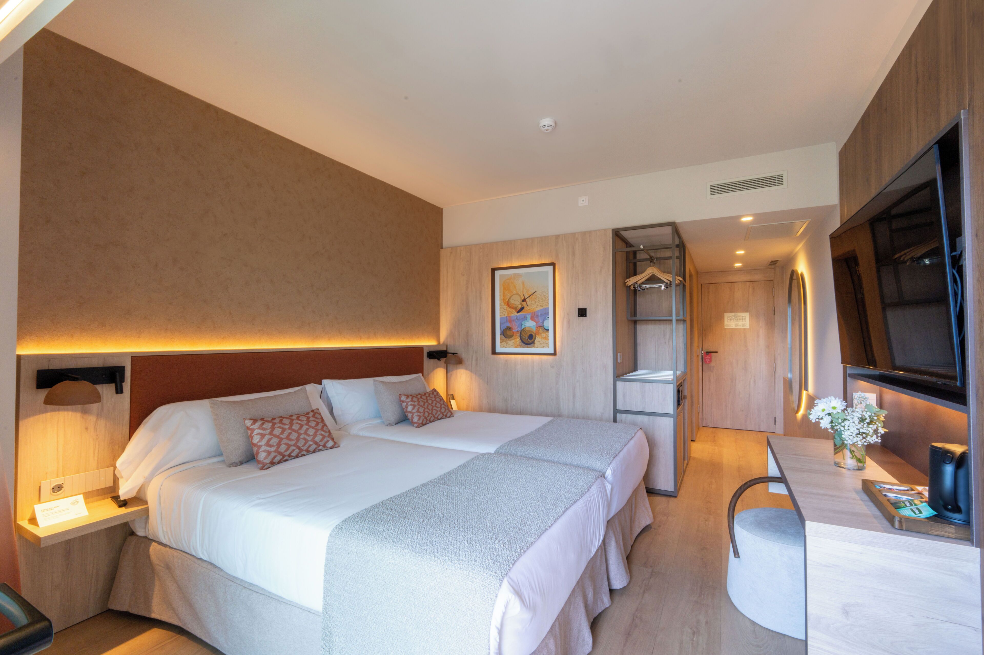 Habitación de hotel con dos camas, un escritorio, un televisor y un espejo.