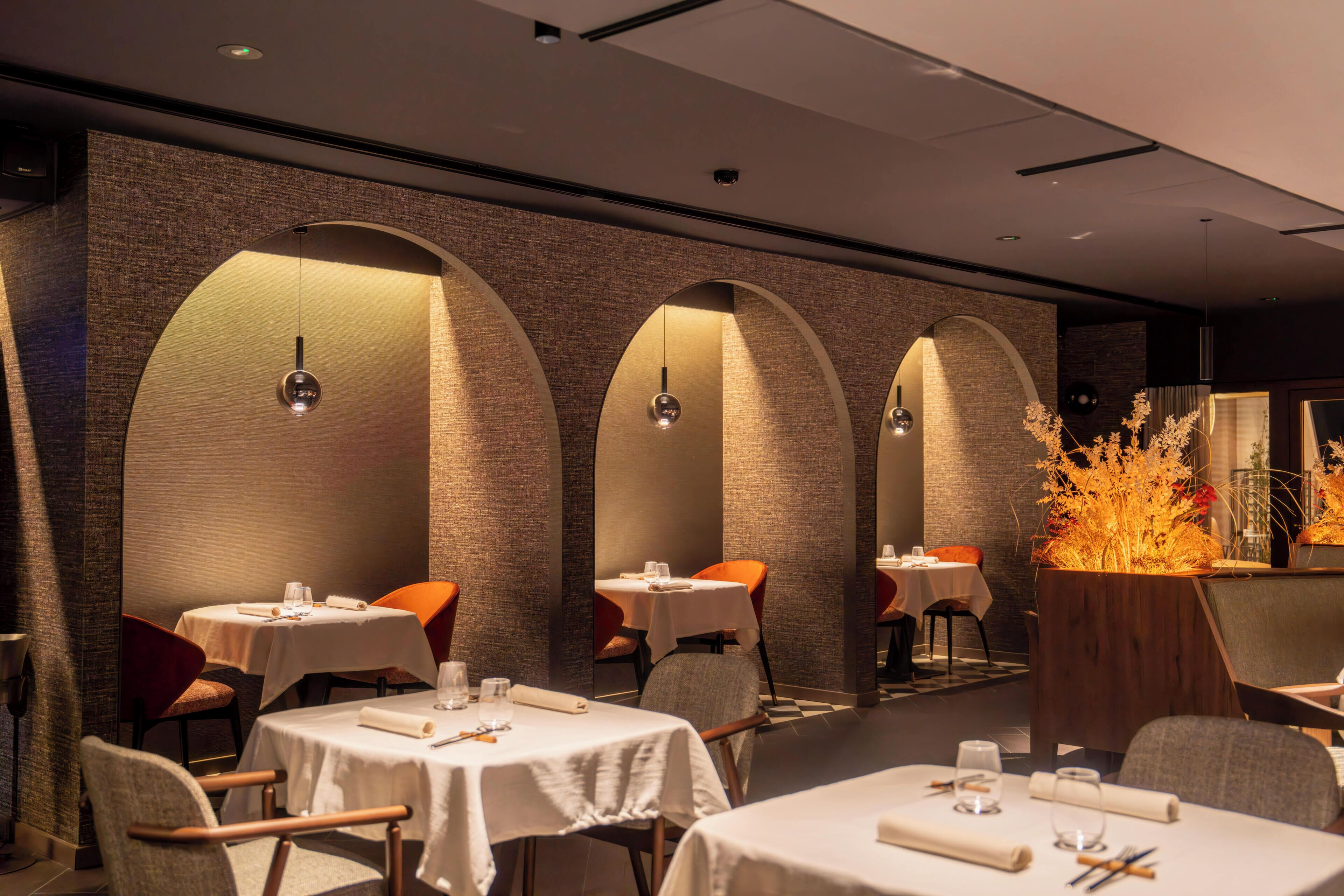 A restaurant with tables, chairs, and a decorative plant arrangement.