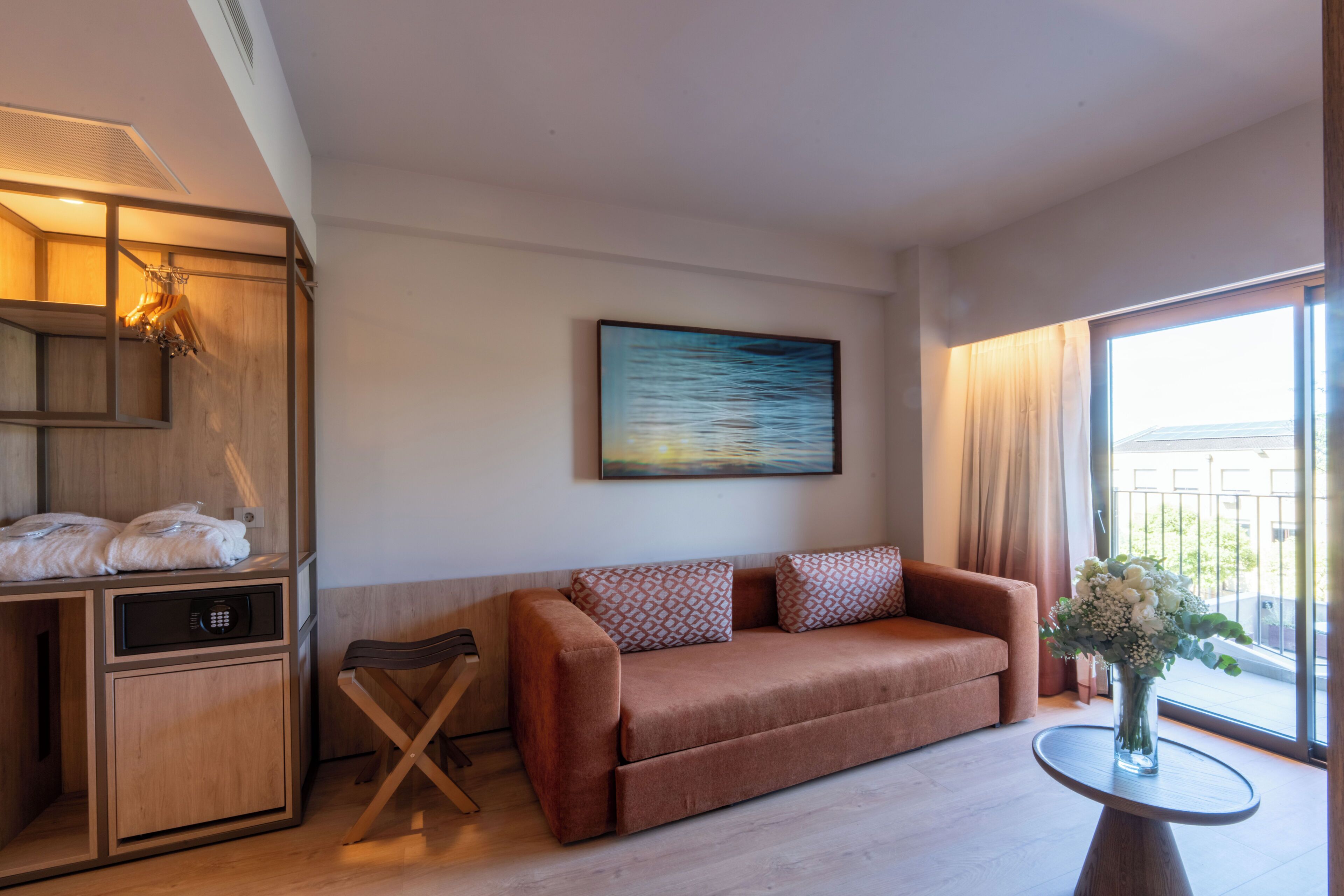 Habitació d'hotel moderna amb un sofà, una taula petita amb un ram, un armari de fusta i un quadre a la paret.