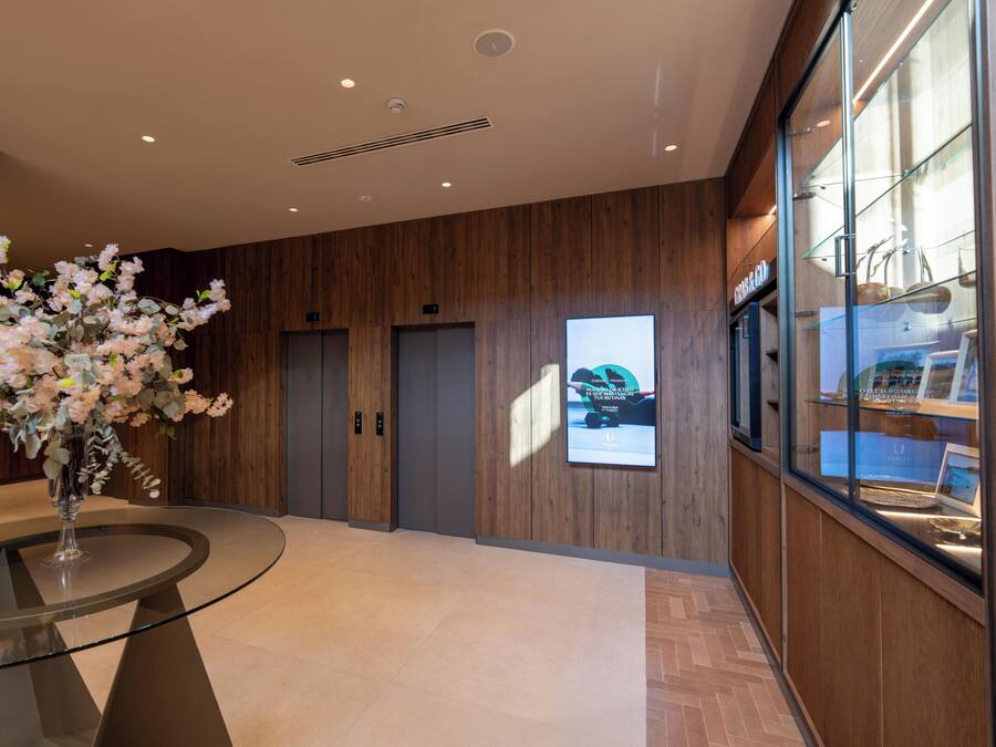 Un vestíbulo moderno con una mesa redonda de vidrio, un arreglo floral, paneles de madera y un ventanal con vistas.