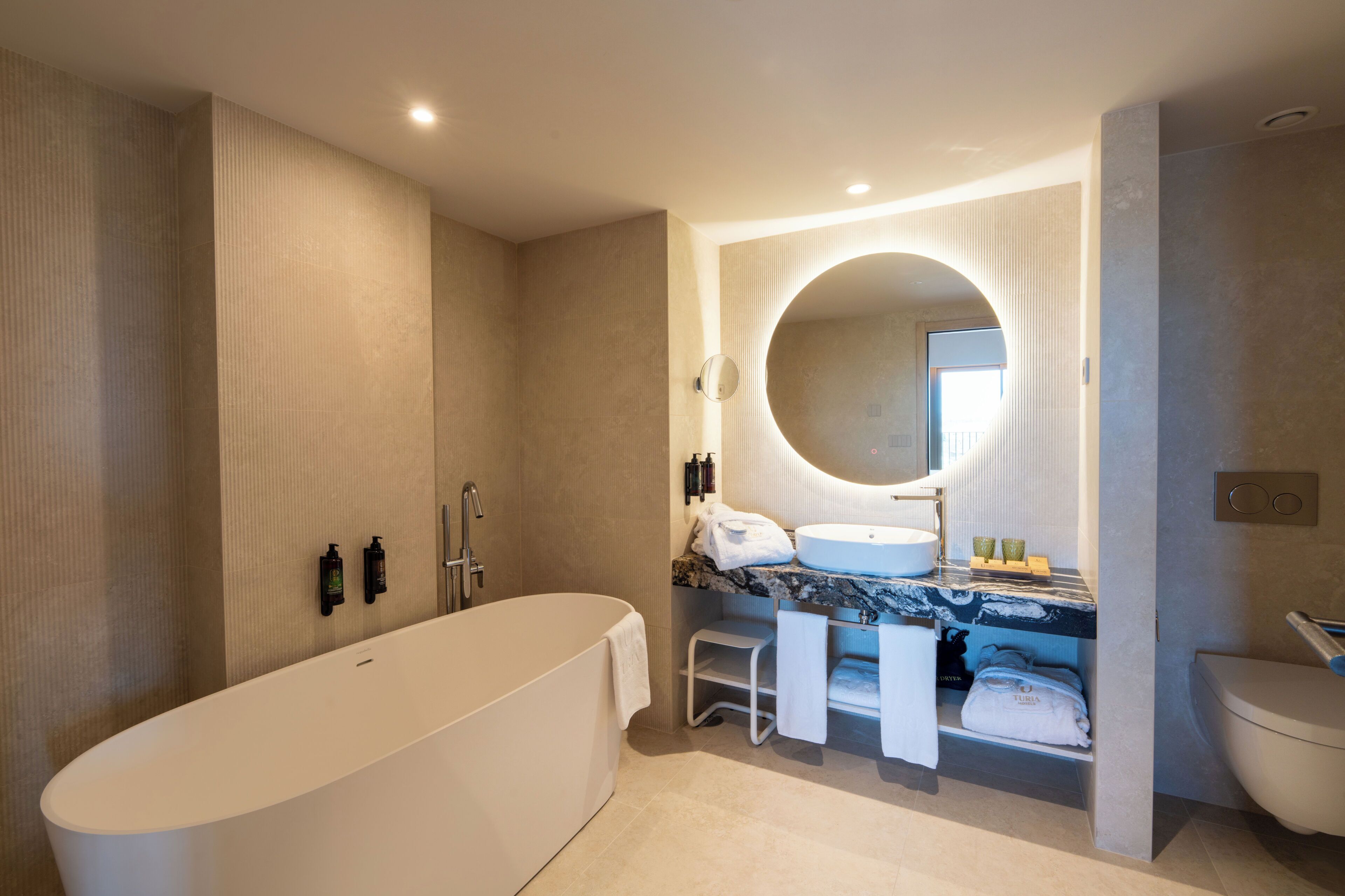 Un baño moderno con una bañera independiente, un espejo grande, un tocador con lavabo y un inodoro.