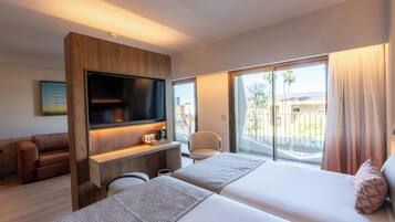 Ein Hotelzimmer mit Fernseher, einer Couch, einem Schreibtisch, einem Stuhl und einem Balkon mit Blick.