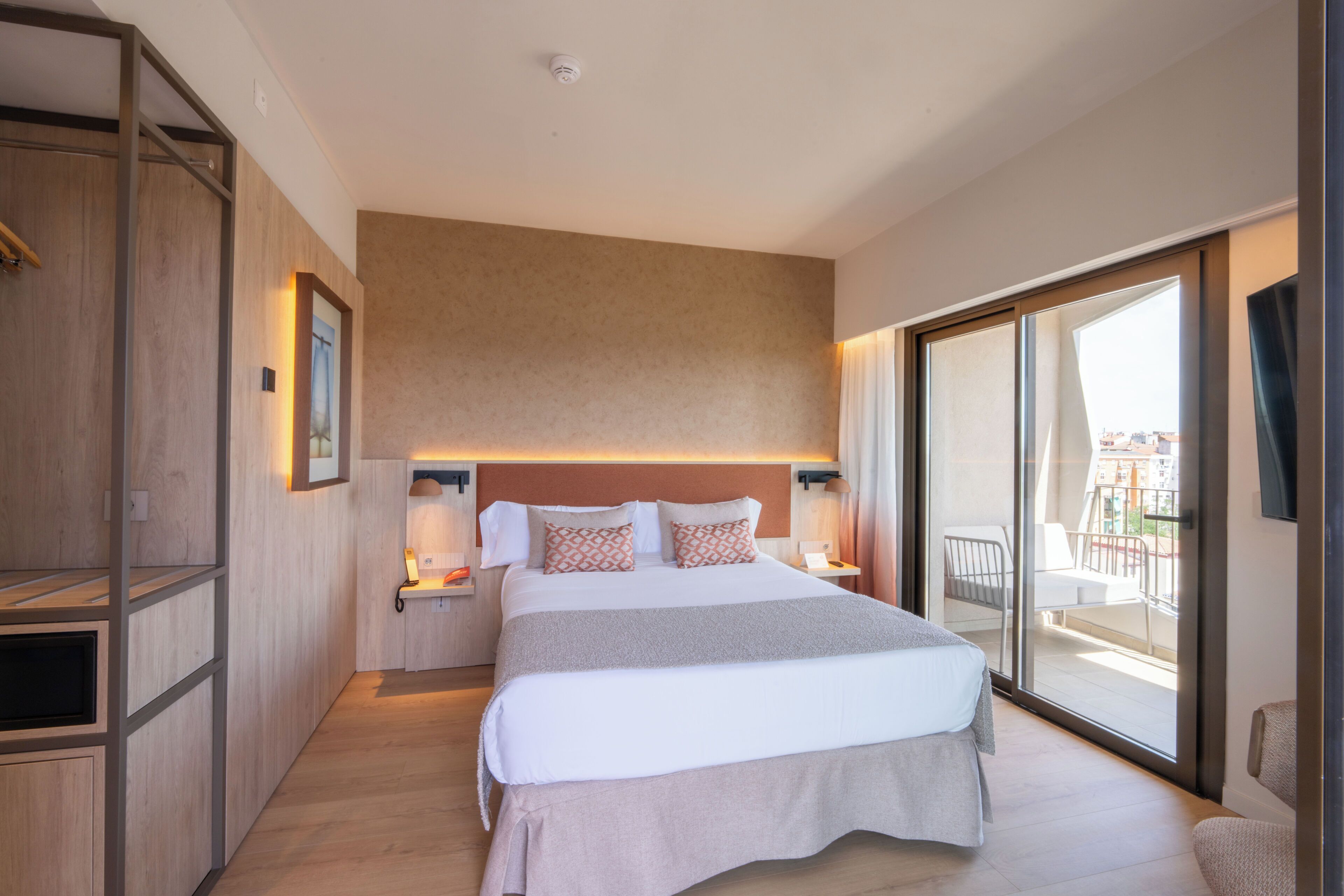 Una habitación de hotel moderna con una cama grande, una puerta corrediza de vidrio a un balcón y un armario de madera.