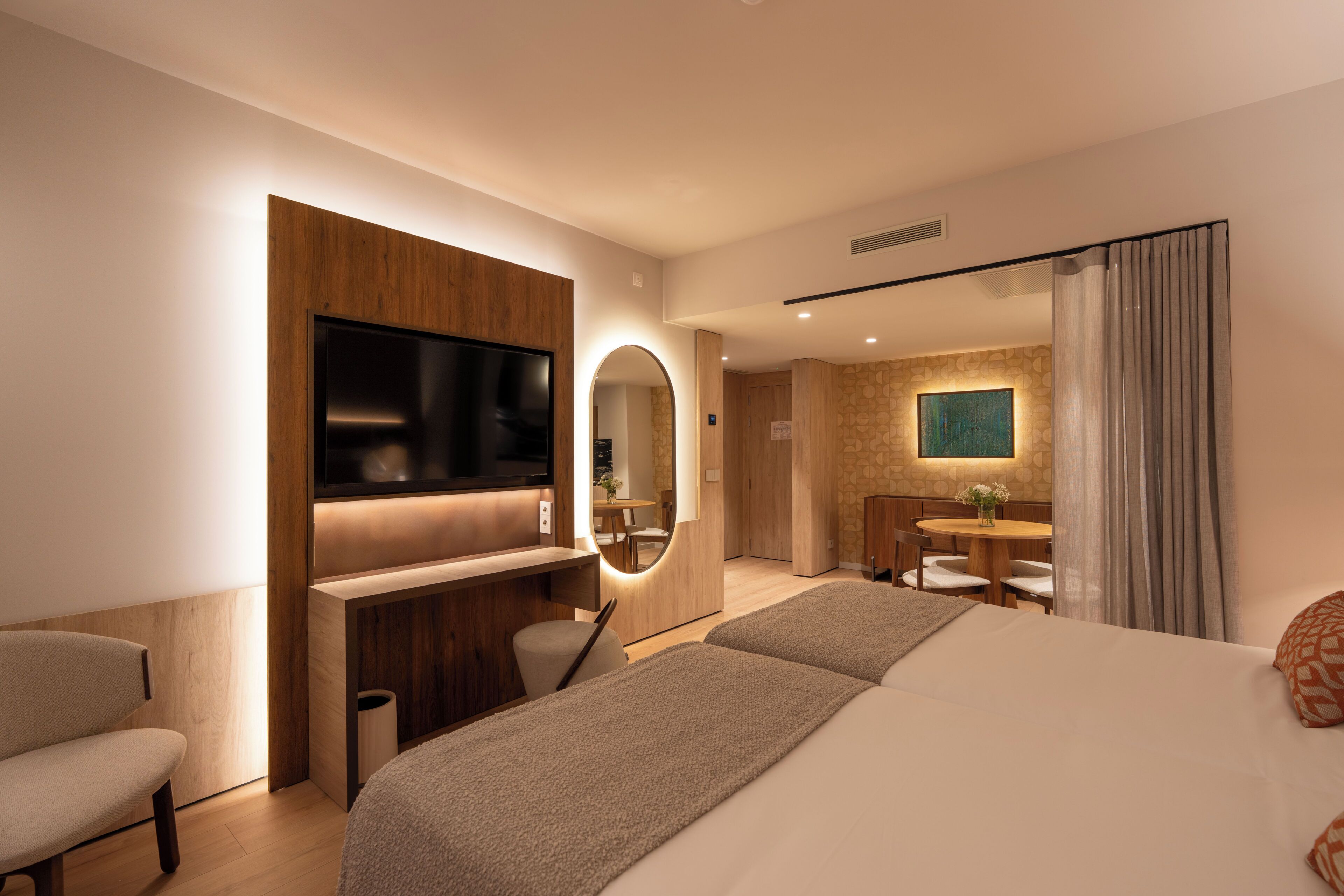 Ein modernes Hotelzimmer mit Bett, Schreibtisch, Stuhl, Fernseher und einem Badezimmer mit Spiegel und Waschbecken.
