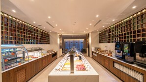 A modern hotel lobby with a central reception desk, a long counter with various amenities, and a wall of glass windows. - Hotel Turia Badajoz (Badajoz)