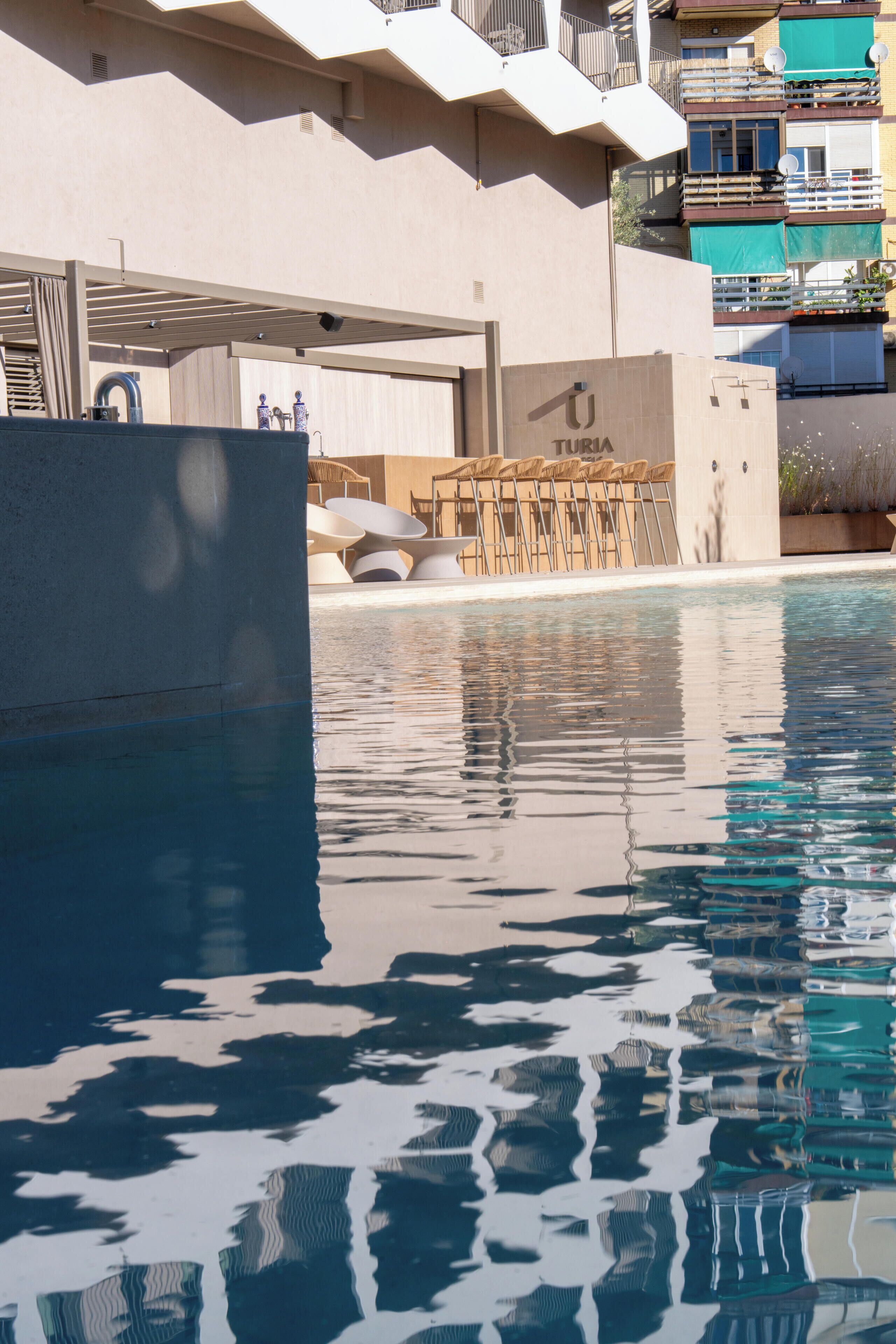 A swimming pool with a clear reflection, a covered seating area, and a building with balconies.