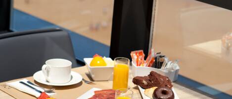 Una mesa de desayuno con vista a la playa, que incluye un plato de comida, una taza, un vaso de jugo de naranja y un bol de fruta.