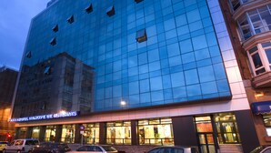 Ein modernes Hotel mit Glasfassade, mehreren Etagen und einem Eingangsbereich mit sichtbarer Beschilderung.