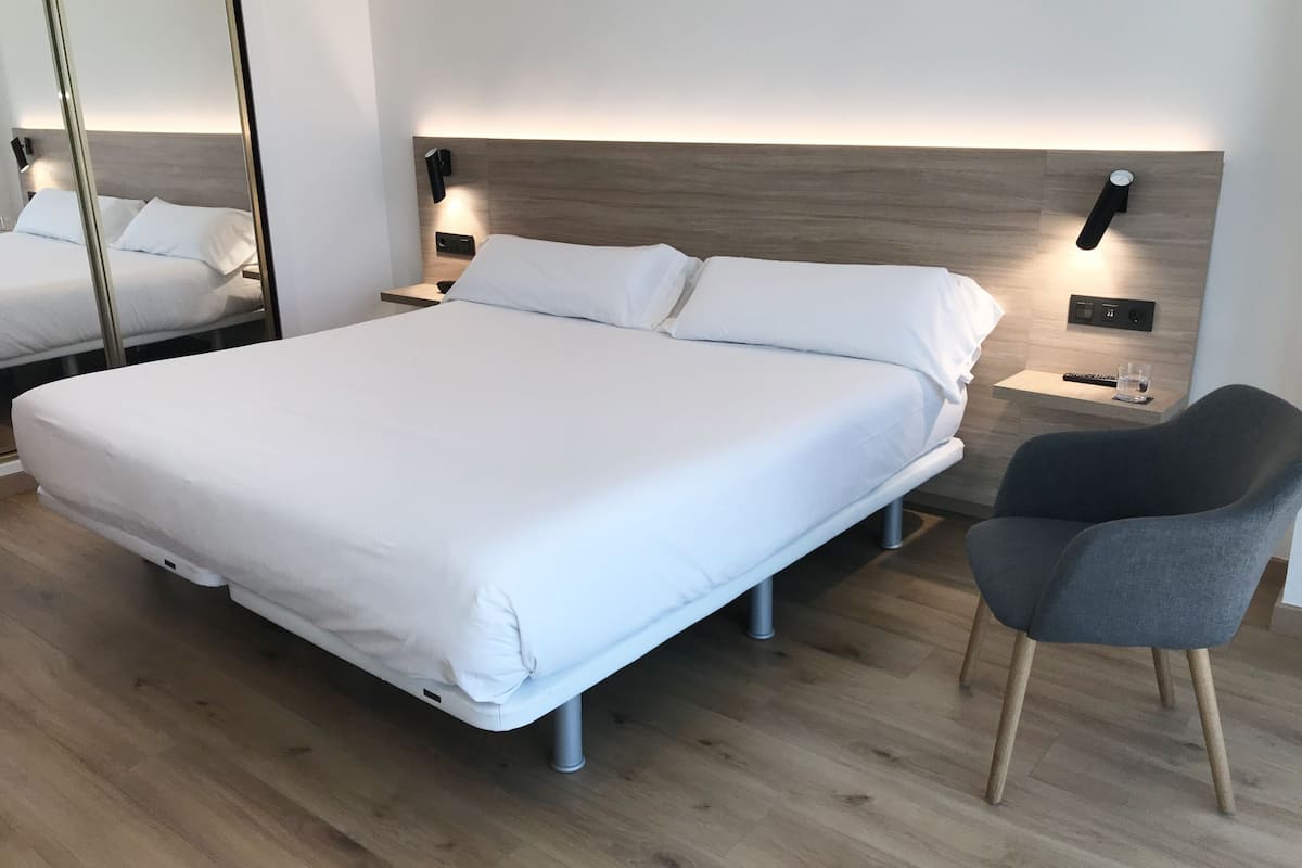 Una habitación de hotel moderna con una cama grande, mesitas de noche, una silla y un espejo.