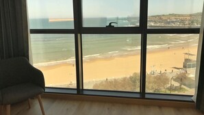 Ein Zimmer mit großem Fenster, Blick auf einen Strand und eine Brücke.