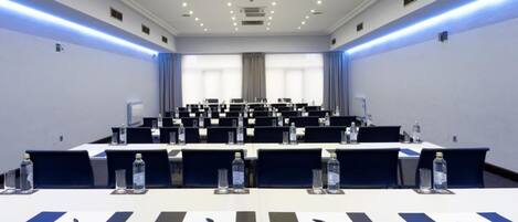 Un salón de conferencias con filas de mesas, sillas y botellas de agua.