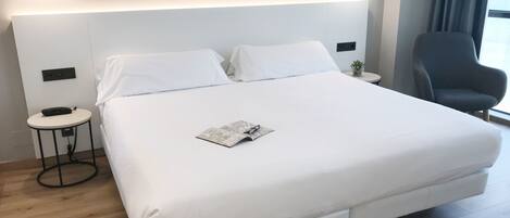 A modern hotel room with a large bed, bedside tables, a chair, and a window with curtains.