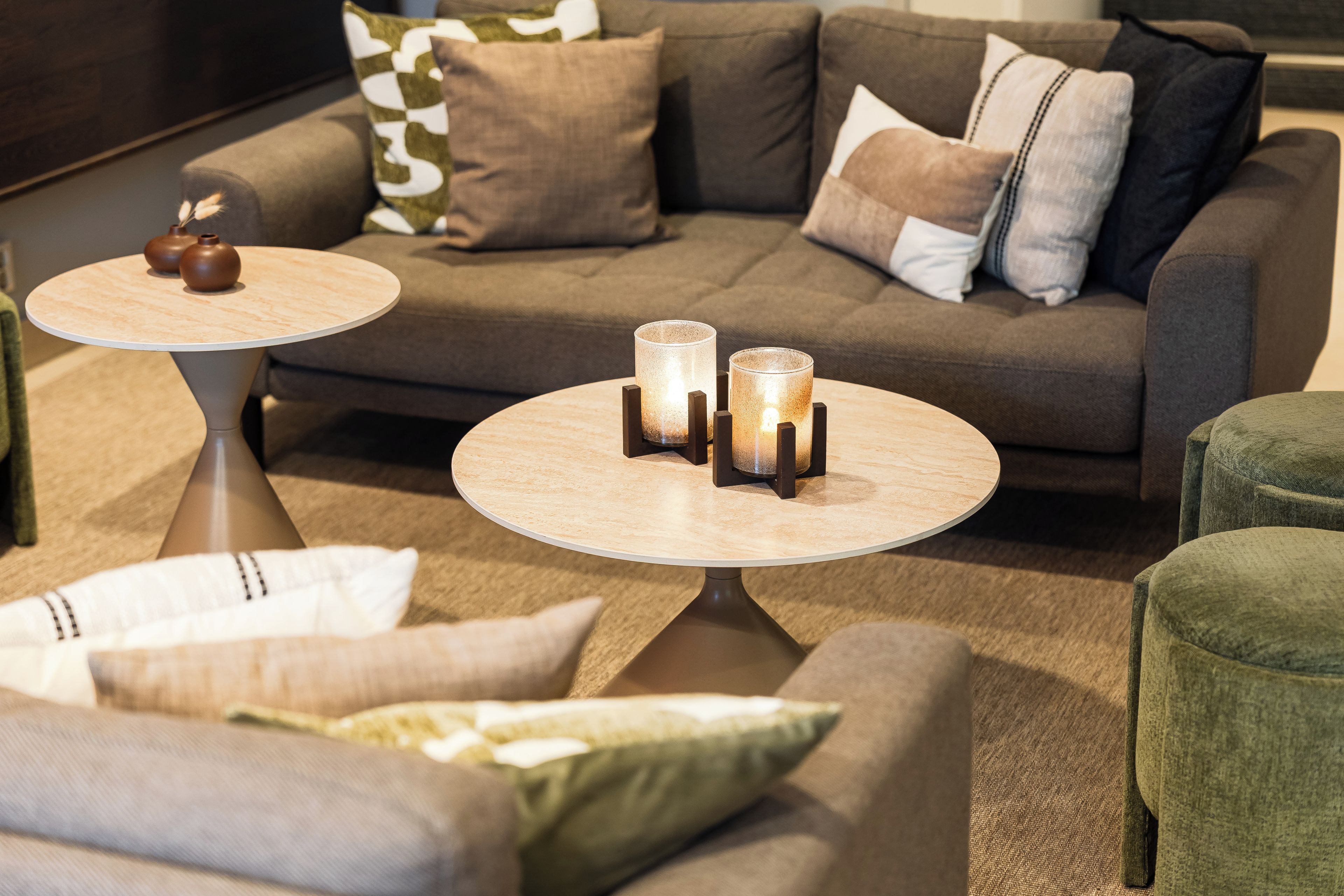A modern living room with a grey sofa, two round tables, and decorative candles.