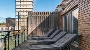 A balcony with four sun loungers, a wooden fence, and a brick wall with a window. - Best Western Malmia Hotel (Skelleftea)