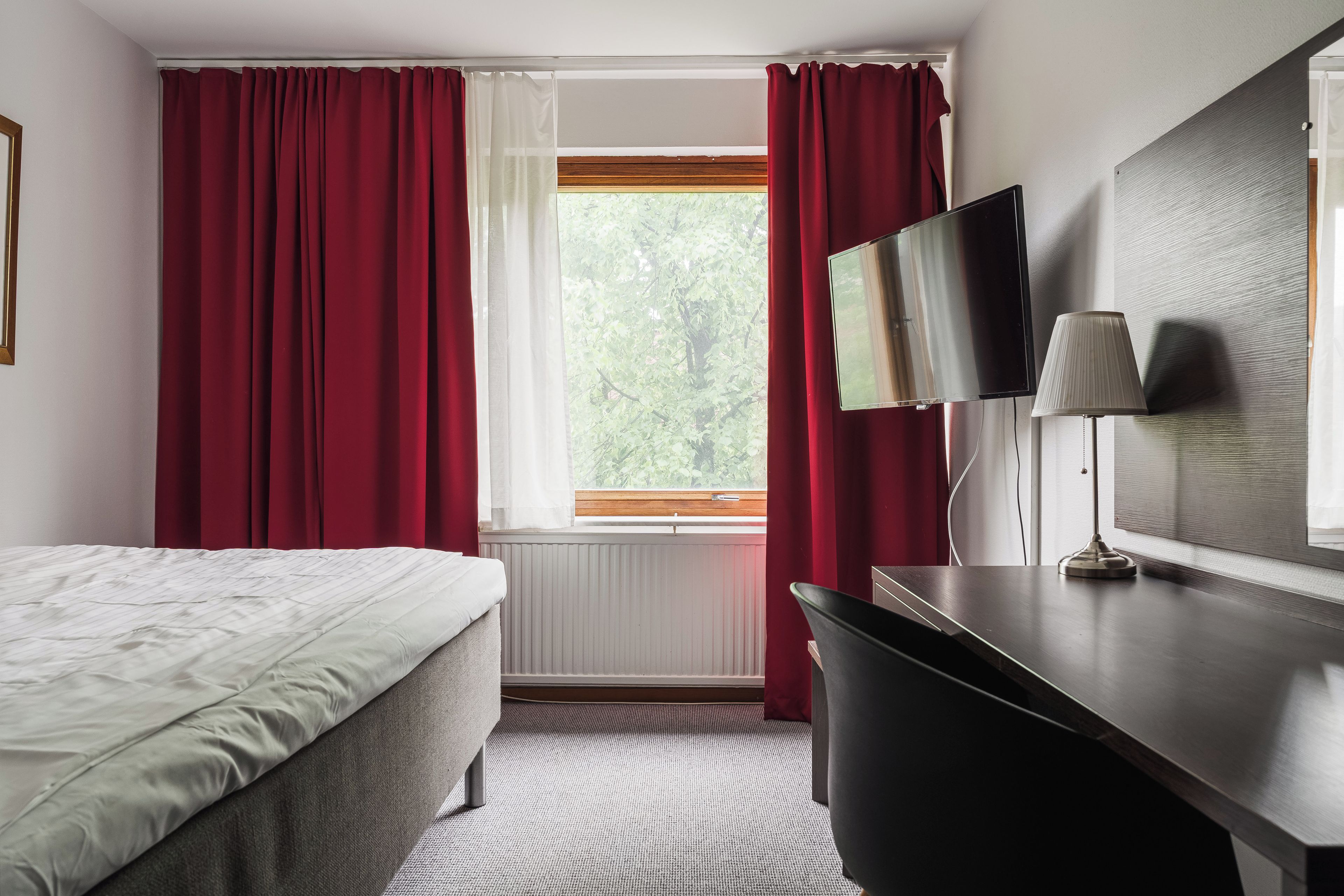Une chambre d’hôtel avec un lit, un bureau, une télévision et une fenêtre avec des rideaux.