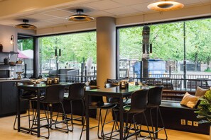 A modern bar area with high stools, a bar counter, and large windows offering a view of the street. - Best Western Malmia Hotel (Skelleftea)