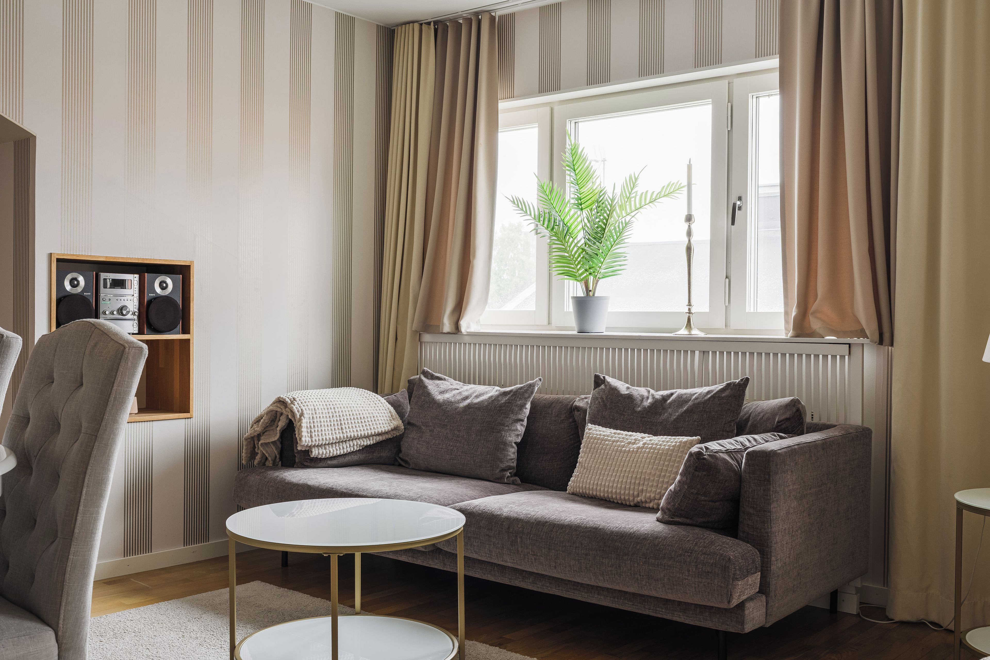 A living room with a sofa, a round coffee table, a potted plant, and a speaker unit.