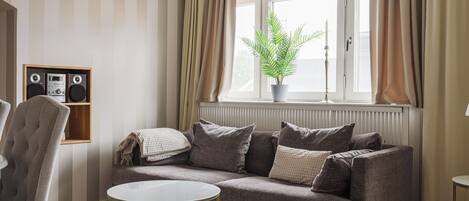 A living room with a sofa, a round coffee table, a potted plant, and a speaker unit.