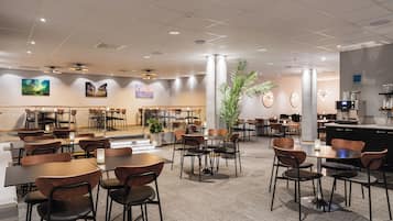 A spacious indoor dining area with multiple tables and chairs, ceiling lights, and wall-mounted artwork.