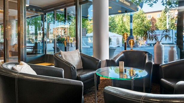 A modern interior with leather furniture, a glass table, and large windows offering a view of the street and buildings outside. - Best Western Malmia Hotel (Skelleftea)