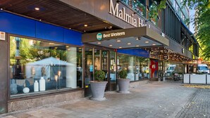 A hotel entrance with a large glass facade, outdoor seating, and potted plants. - Best Western Malmia Hotel (Skelleftea)